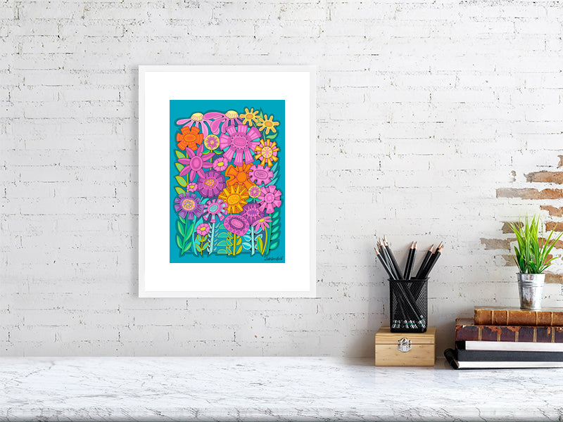 Framed colorful floral artwork on a white brick wall above a desk.