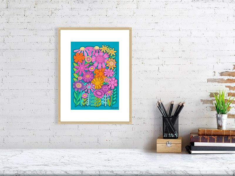 Colorful floral artwork in an oak frame on a white brick wall above a desk.
