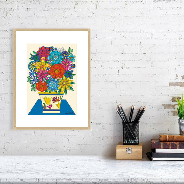 Framed colorful floral artwork on a white brick wall with desk items below.