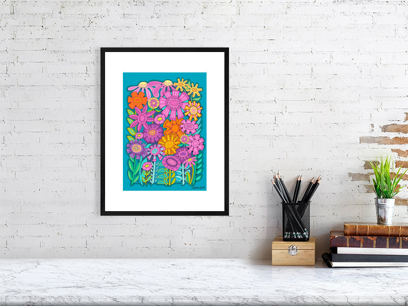 Framed colorful floral artwork on a white brick wall above a desk.