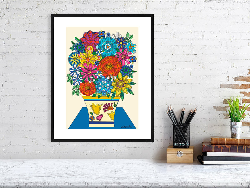 colorful floral artwork in a black frame with a white matt border on a white brick wall with desk items below.