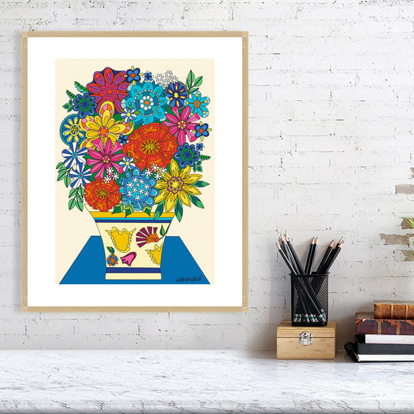 Framed colorful floral artwork on a white brick wall with a desk in the foreground.