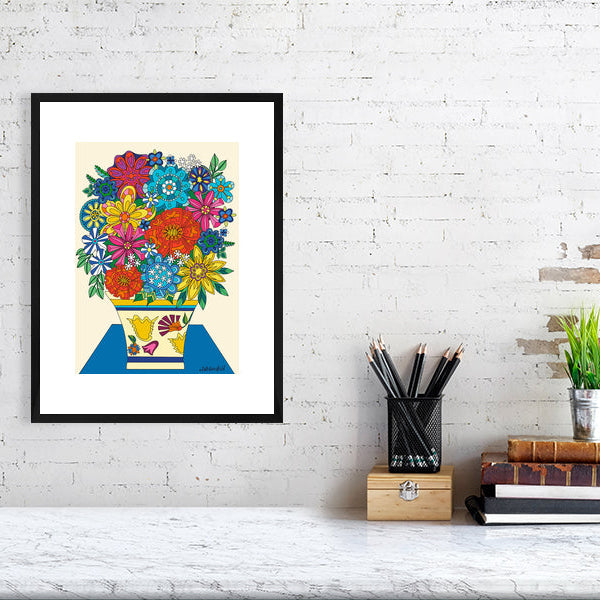 Framed colorful floral artwork on a white brick wall with desk items below.