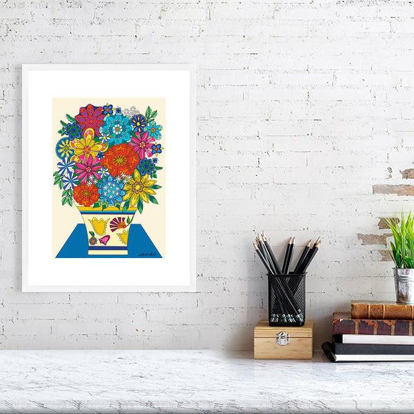 Framed colorful floral artwork on a white brick wall above a desk.