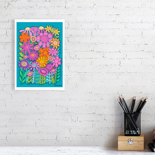 Colorful floral 'Fabulous Flowerbed' art print bu Uk artist Ruth DRonsfield. On a white brick wall above a desk with stationery items.