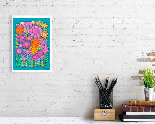 Colorful floral 'Fabulous Flowerbed' art print bu Uk artist Ruth DRonsfield. On a white brick wall above a desk with stationery items.