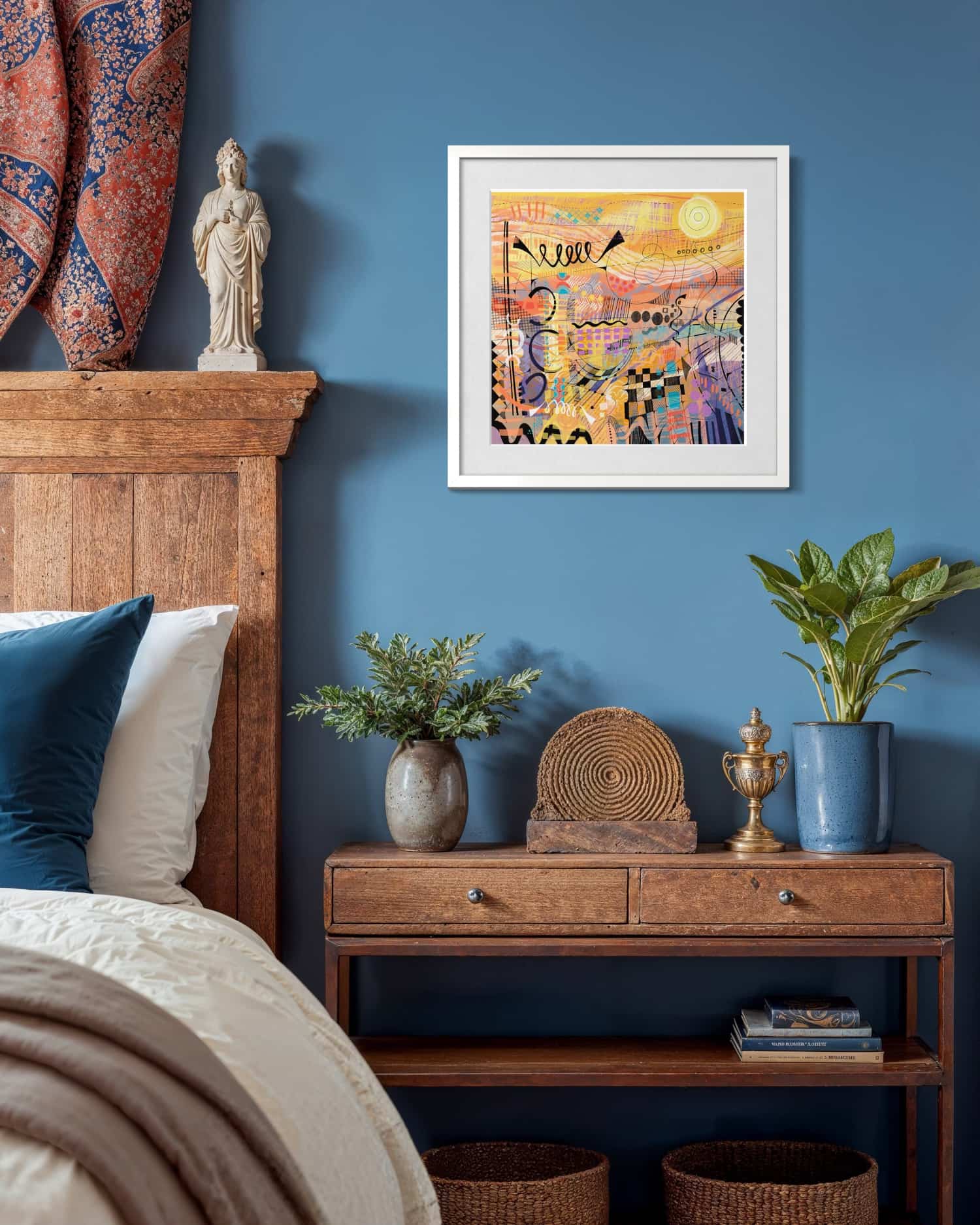 sunburst giclee art print by UK artist Ruth Dronsfield shown in a bedroom with wooden headboard, nightstand, and blue wall.